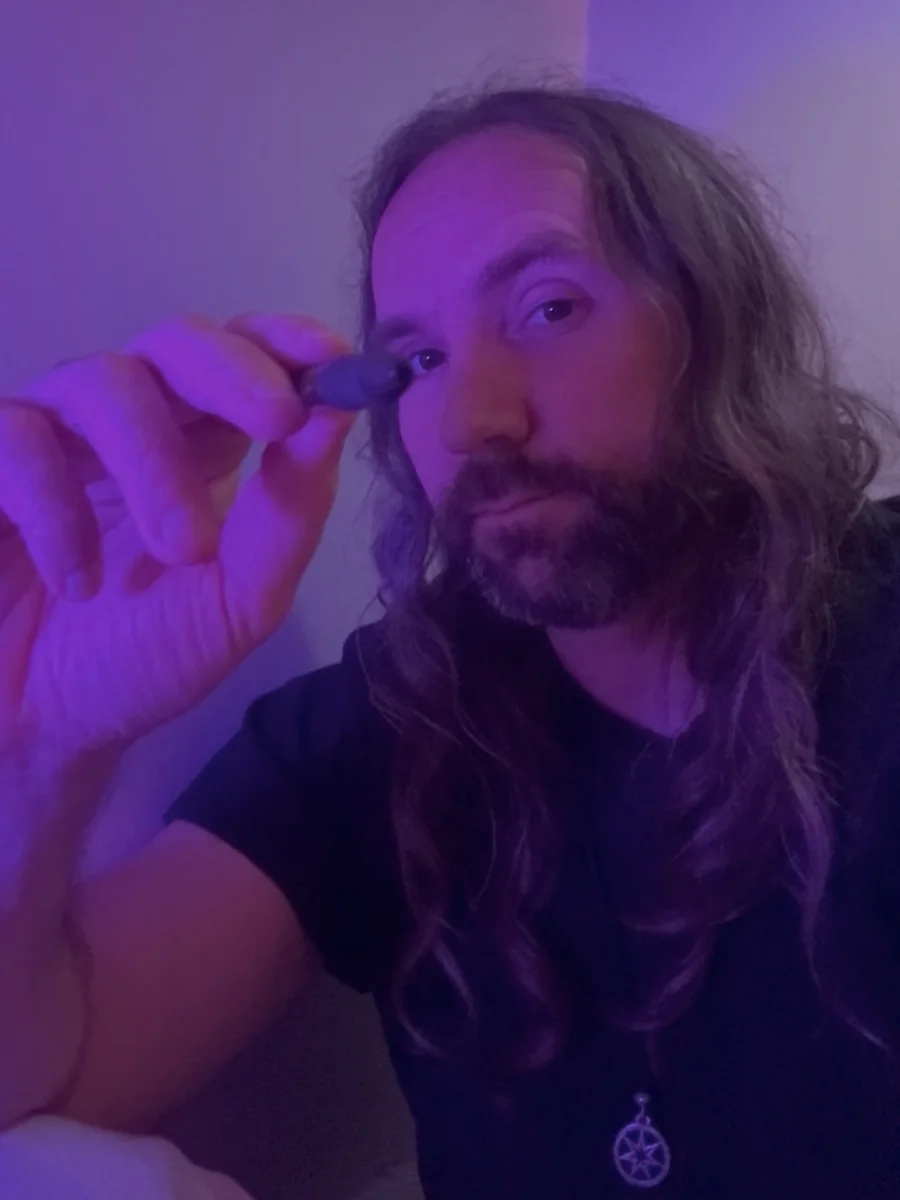 Jay Cook, the writer of Weeping For Waves, holding a pen in violet light